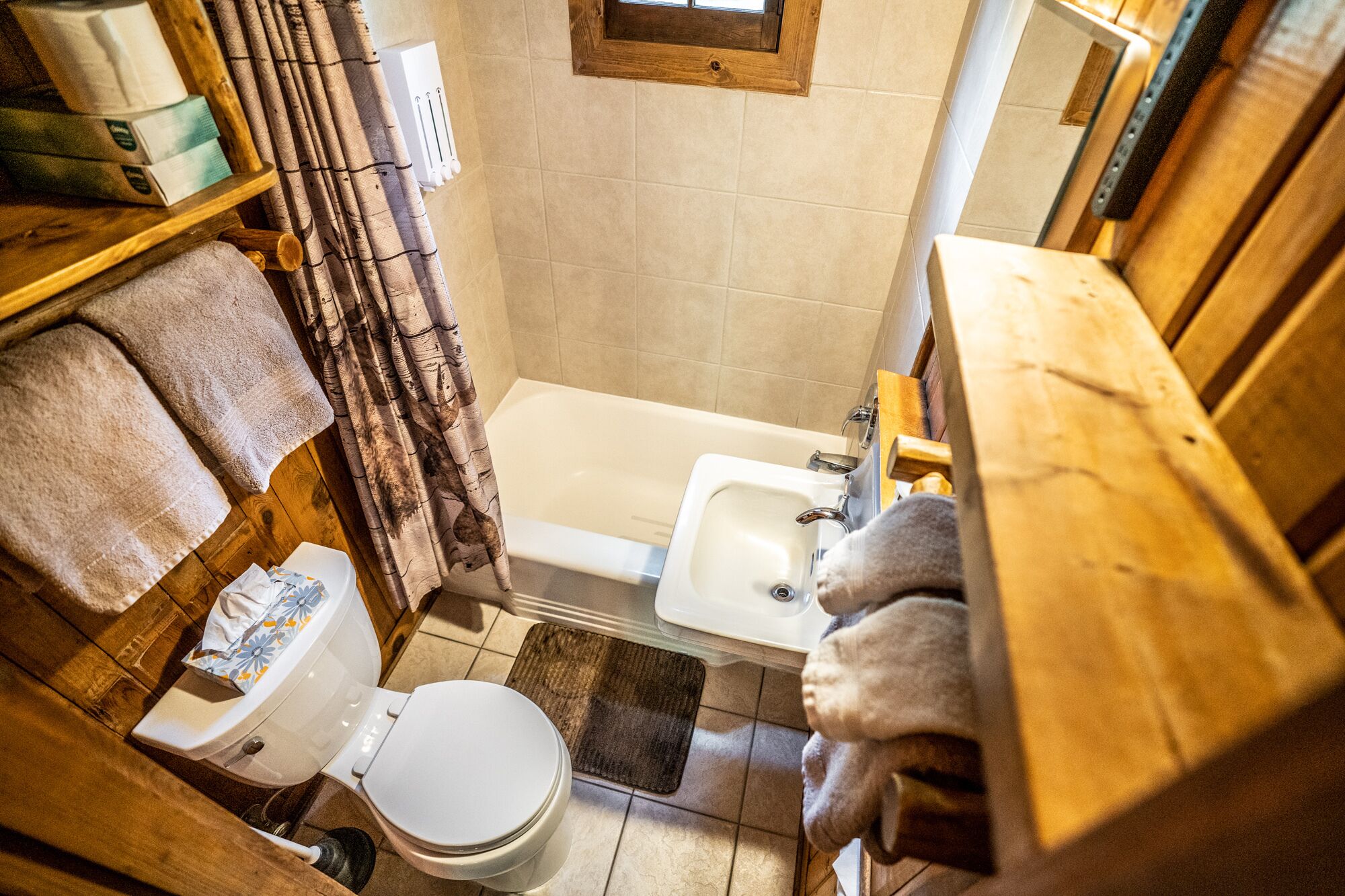 Une petite salle de bain comprenant des toilettes, un lavabo et une baignoire. On y trouve des serviettes et une petite fenêtre située au-dessus de la baignoire.
