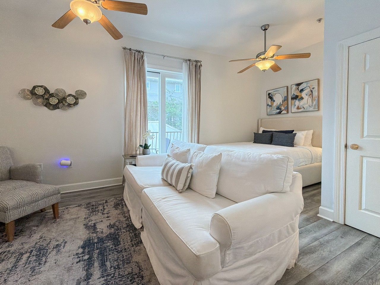 A bedroom with a white sofa, a bed, two ceiling fans, and a window with curtains.