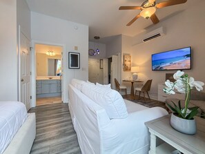 Ein modernes Hotelzimmer mit einer Couch, einem Esstisch, einem Fernseher und einer Küche im Hintergrund.