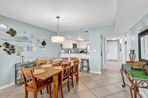 Un comedor con mesa y sillas de madera, una cocina al fondo y un pasillo que conduce a otra habitación.