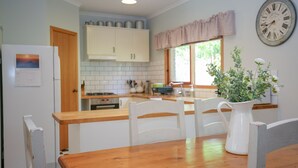Eine Küche mit weißen Schränken, einer Holzausziehtafel und einem Essbereich mit weißem Tisch und Stühlen.