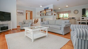 Ein Wohnzimmer mit gestreiften Sofas, einem Couchtisch, einem Fernseher und einem durchgehenden Durchgang zur Küche.