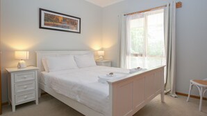 Ein ordentlich eingerichtetes Schlafzimmer mit einem Bett, zwei Nachttischen, einem Schreibtisch, einem Stuhl und einem Fenster mit Vorhängen.