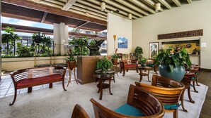 Un vestíbulo con muebles de madera, plantas en macetas y vistas al exterior.