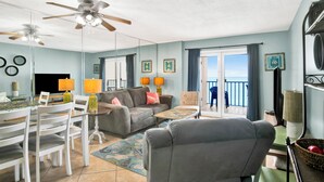 A living room with a ceiling fan, a dining table with chairs, a sofa, and a view of the ocean through a sliding door.