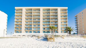 A multi-story hotel with balconies, a sandy beach in front, and palm trees.