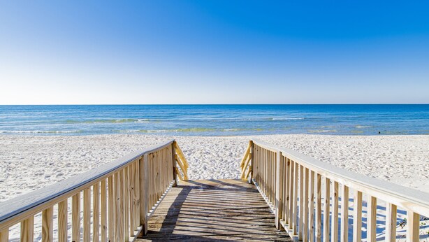 A wooden boardwalk leading to a sandy beach with clear blue water.