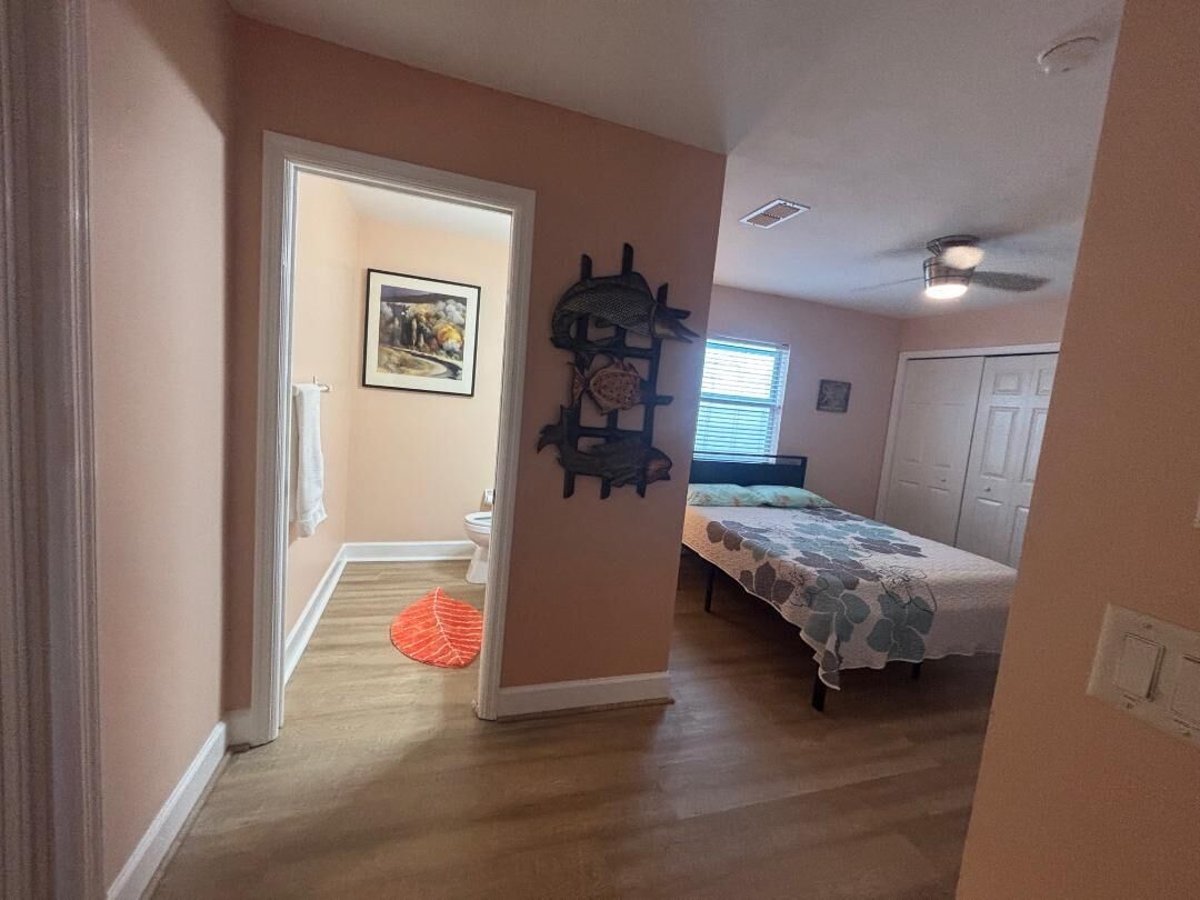 Een slaapkamer met een bed, een plafondventilator en een deur naar een andere kamer.