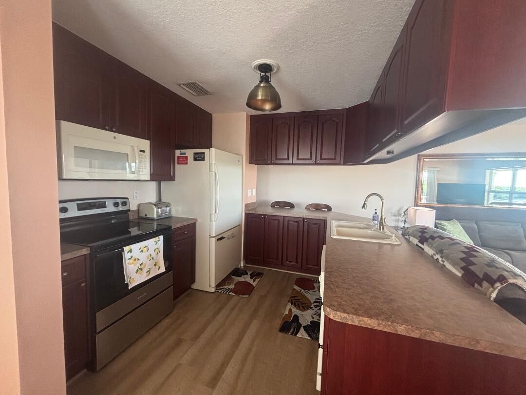 A compact kitchen with dark wood cabinets, a microwave, stove, refrigerator, and a sink.