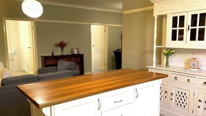 A kitchen with white cabinets, a wooden countertop, and a dining area with a grey sofa. - Dora Hall | Very Central (Orange)