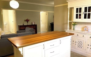 A kitchen with white cabinets, a wooden countertop, and a dining area with a grey sofa. - Dora Hall | Very Central (Orange)