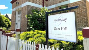A brick building with a sign for 'Dora Hall' and a website address. - Dora Hall | Very Central (Orange)
