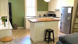 A kitchen with a central island, a refrigerator, a microwave, and a sink. - Dora Hall | Very Central (Orange)
