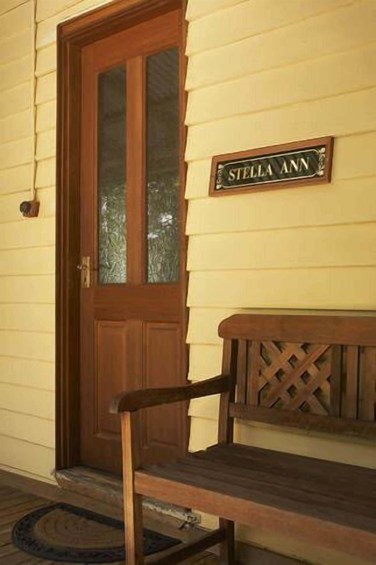 A wooden bench in front of a door with a sign that reads "STELLA ANN".