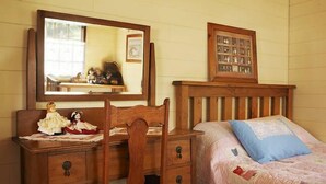 Een slaapkamer met een houten dressoir, een bed met sprei, een spiegel en een lijst met afbeelding aan de muur.