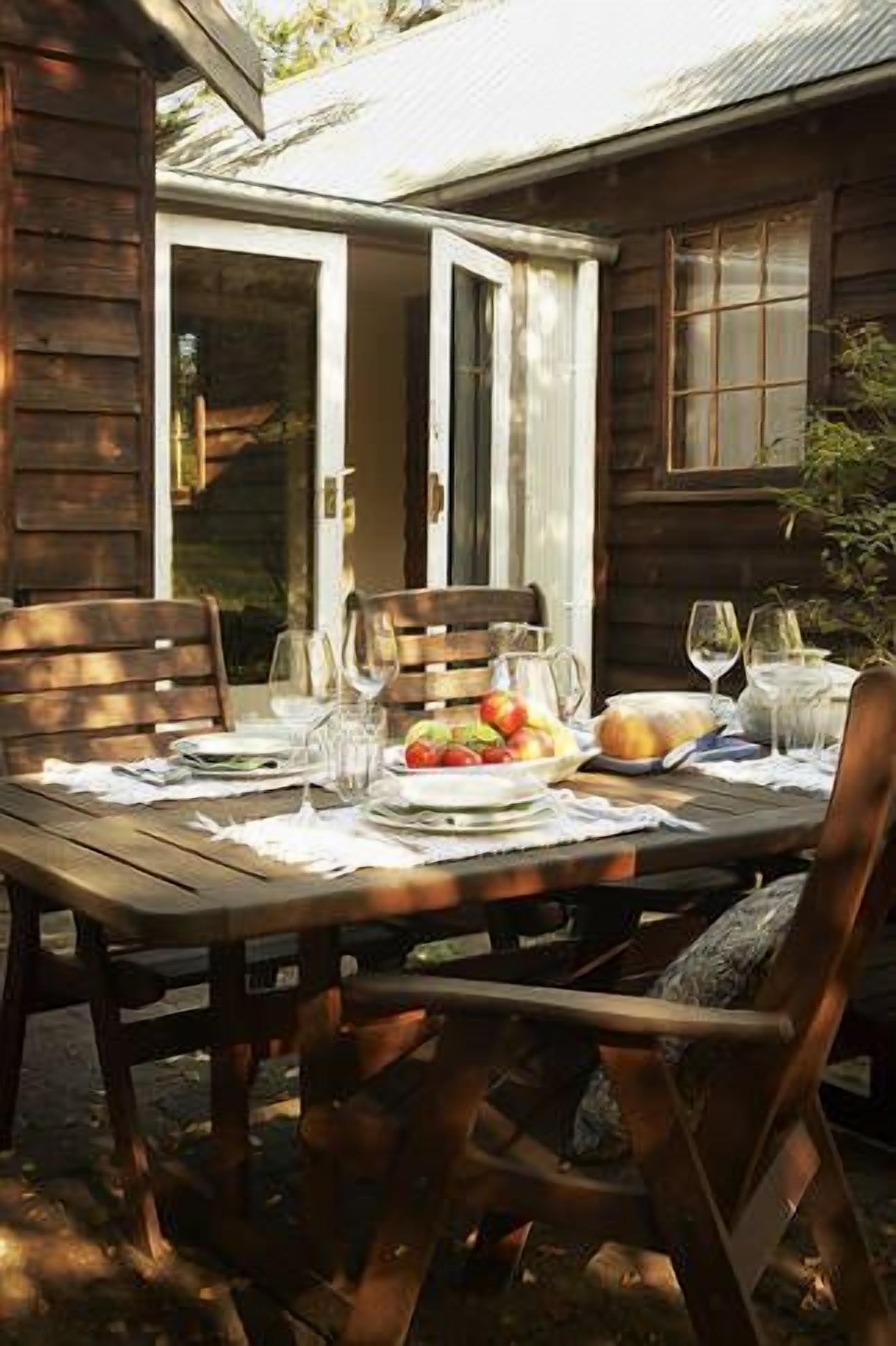A wooden dining table set for two with a fruit bowl, wine glasses, and a pitcher.
