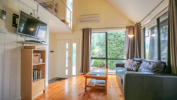 A spacious living room with a wooden floor, a sofa, a coffee table, and a TV mounted on the wall. - ALLAMBIE COTTAGES - VILLA 1: Bright (Bright)