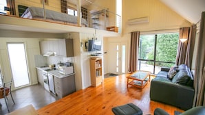 A spacious living area with a sofa, a dining table, and a kitchen with a TV. - ALLAMBIE COTTAGES - VILLA 1: Bright (Bright)