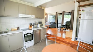 A modern kitchen with a stove, microwave, and sink. There is a dining area with a table and chairs. - ALLAMBIE COTTAGES - VILLA 1: Bright (Bright)