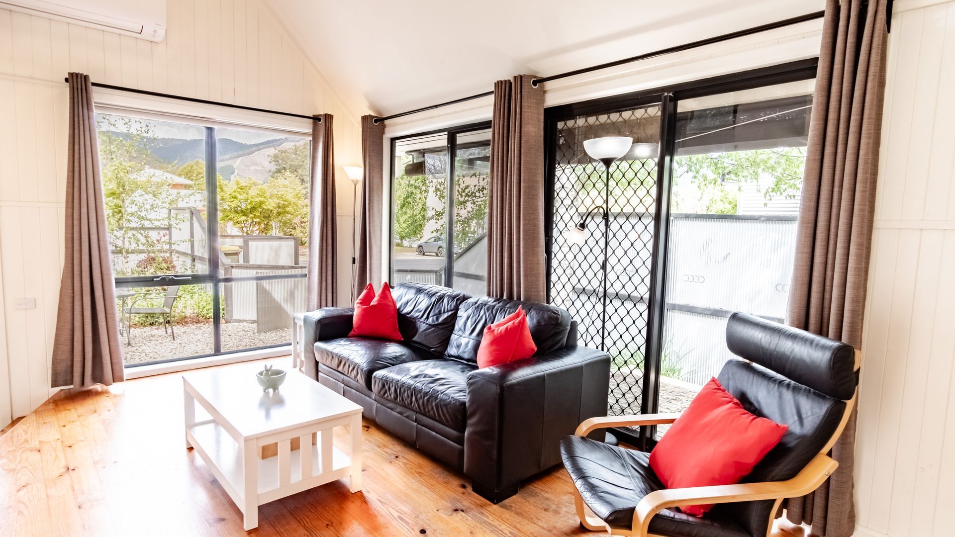 A room with a black leather sofa, a wooden chair, and a white coffee table.