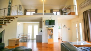 A spacious living area with a high ceiling, a staircase leading to an upper level, a dining area, and a kitchen. - ALLAMBIE COTTAGES - VILLA 1: Bright (Bright)