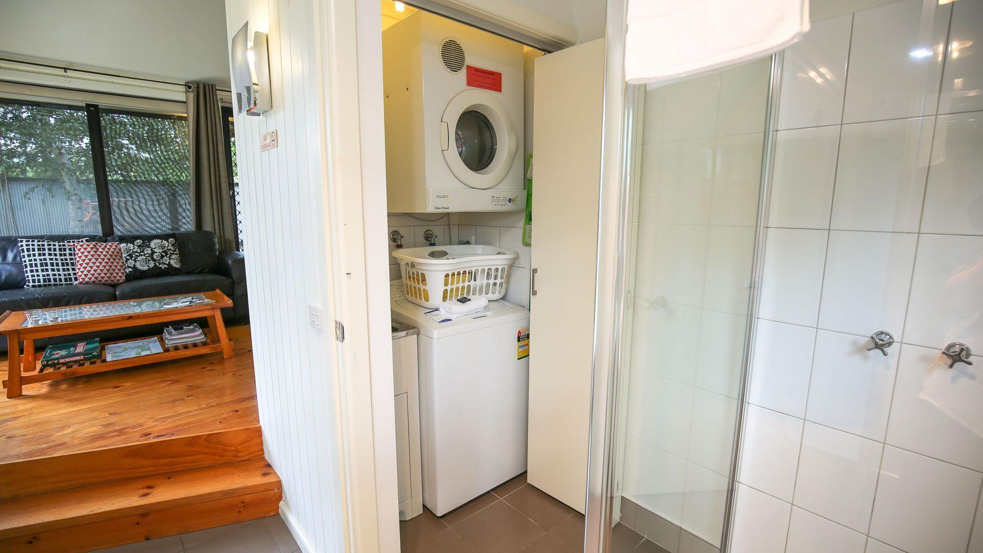 A compact living space with a washing machine, a small laundry basket, a sofa with cushions, and a wooden coffee table.
