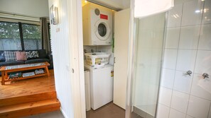 A compact living space with a washing machine, a small laundry basket, a sofa with cushions, and a wooden coffee table.