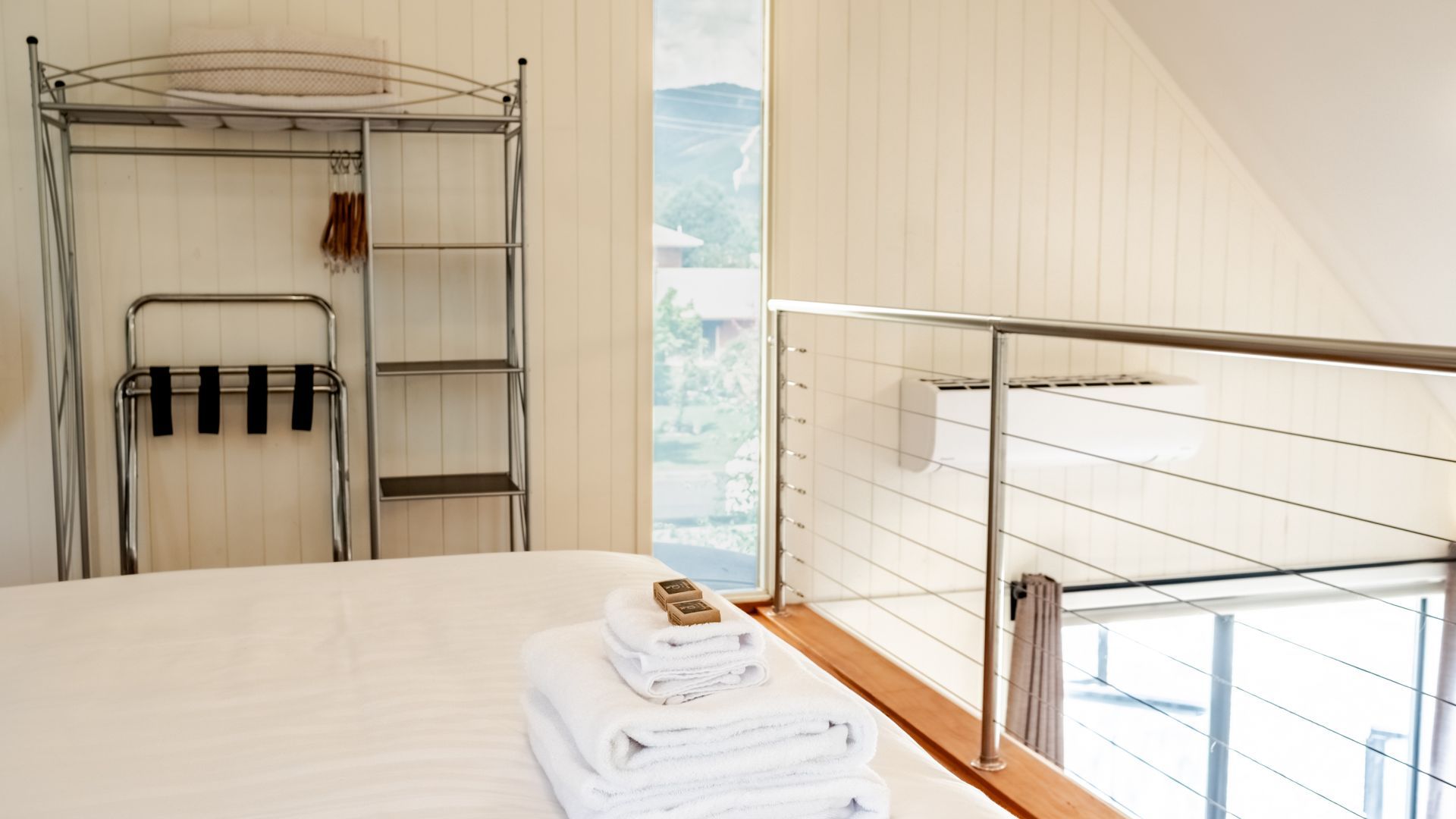 Ein Hotelzimmer mit einem Bett, einem Metallregal mit Handtüchern und Blick ins Freie.
