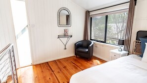 Ein Schlafzimmer mit einem Bett, einem Sessel, einem Nachttisch, einem Spiegel und einem Fenster mit Vorhängen.