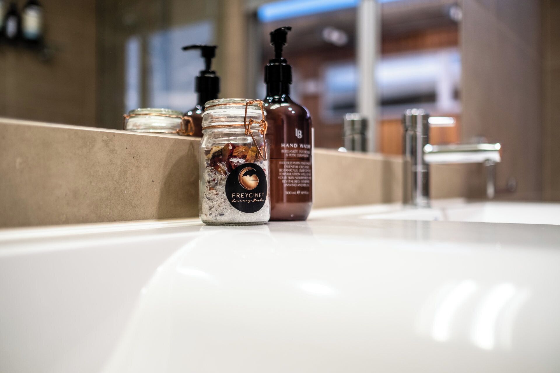 A bathroom sink with a jar of hand wash soap and a bottle of hand wash cream.