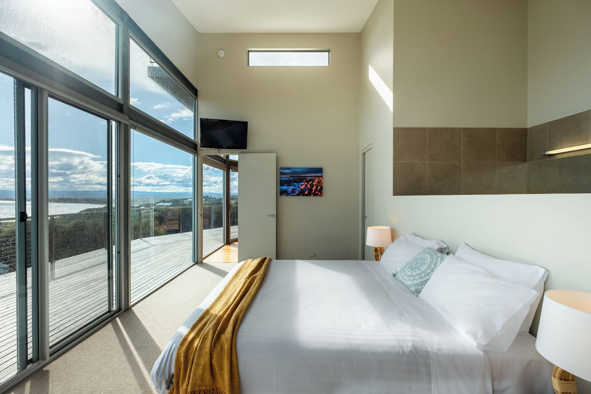 A modern hotel room with a large bed, a TV mounted on the wall, and a view of the city through large windows.