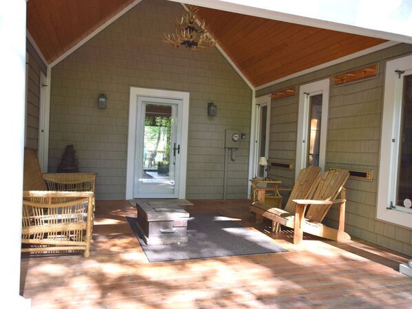 A covered porch with wooden flooring, wicker furniture, and a chandelier.
