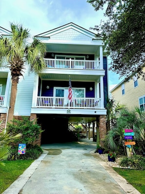 A two-story building with a balcony, an American flag, and a sign indicating nearby locations. - Make memories in this spacious home, short walk to the beach and Surfside Pier. (Surfside Beach)