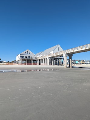 A coastal building with a covered walkway and a beach in the foreground. - Make memories in this spacious home, short walk to the beach and Surfside Pier. (Surfside Beach)
