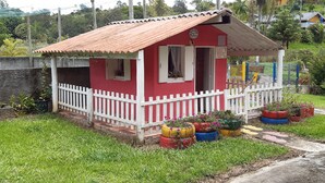 A small red house with a white picket fence, surrounded by green grass and potted plants. - Leisure and Rest for any day (Guararema)