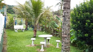 A garden with a white table and four stools, surrounded by palm trees and a dense bush. - Leisure and Rest for any day (Guararema)