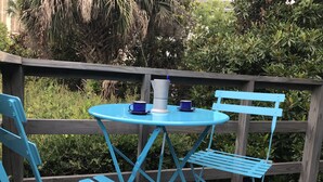 Mesa y sillas de metal azul sobre una terraza de madera con vista a zonas verdes.