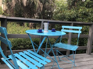 Ein blauer Metalltisch und -stühle auf einer Holzterrasse mit Blick ins Grüne.