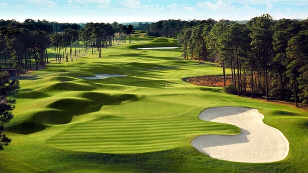 Campo de golf con búnkeres de arena, árboles y cielo despejado.