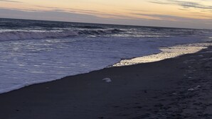 Una playa con olas rompiendo sobre la orilla, bajo un cielo parcialmente nublado.