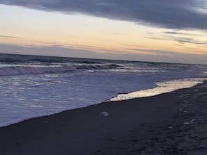 Ein Strand mit brechenden Wellen, unter einem teils bewölkten Himmel.