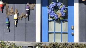 Una puerta azul con un adorno de guirnalda morada, pared azul y blanca, y faroles decorativos.