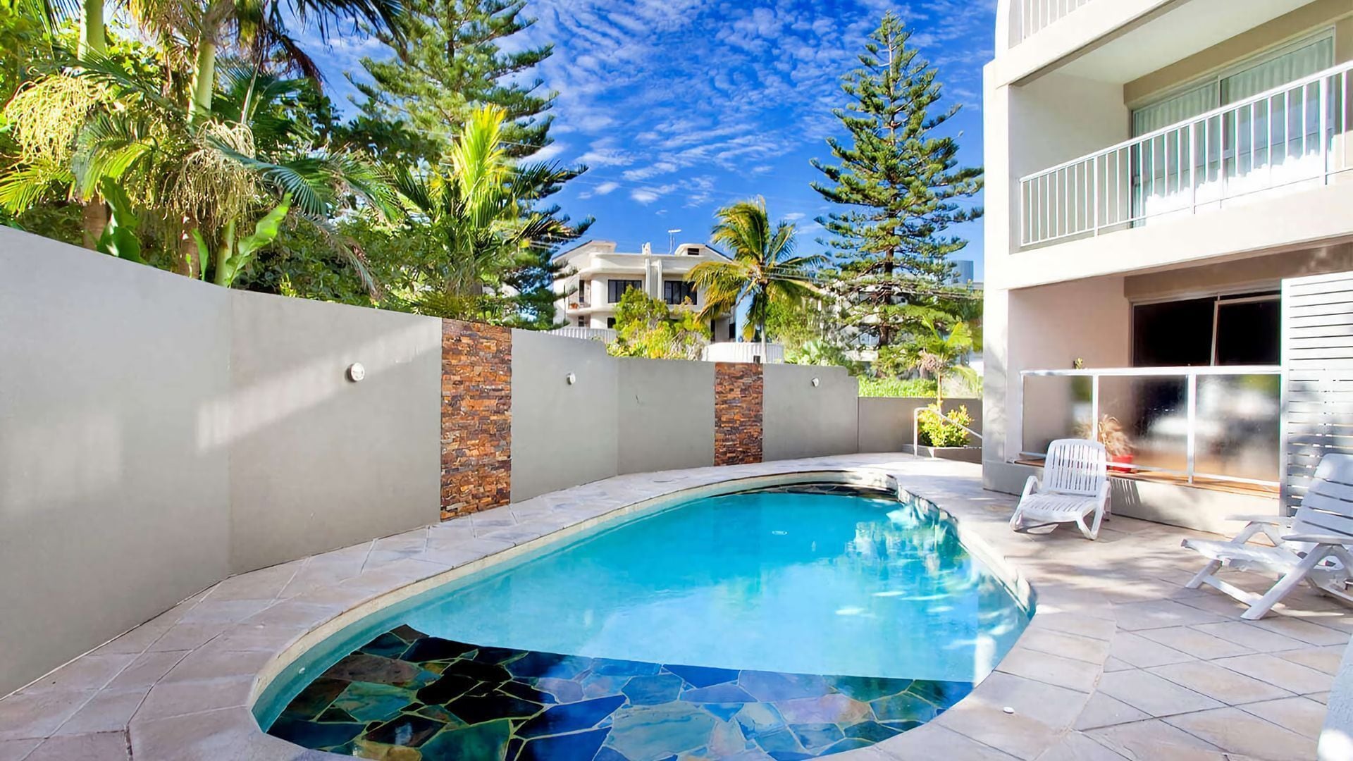 Una piscina con diseño de mosaicos, rodeada por un muro bajo y una valla blanca.