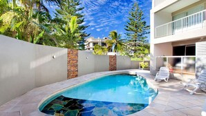 Une piscine dont le fond est décoré de mosaïques, entourée d’un petit muret et d’une clôture blanche.