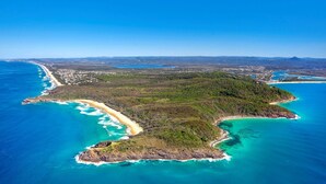 Vue aérienne d’une zone côtière comprenant une plage, une zone boisée et une petite ville en arrière-plan.