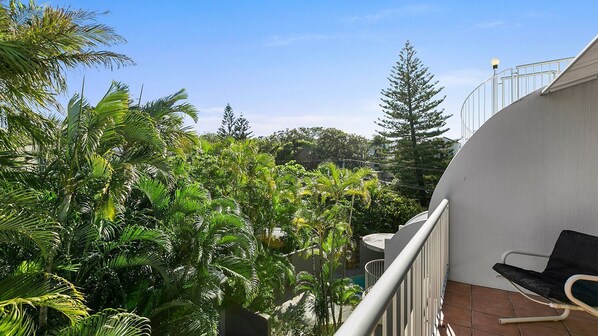 A balcony with a chair, surrounded by lush greenery and a clear blue sky. - Cascades - Top Floor Apartment In Prime Position (SUNSHINE BEACH)