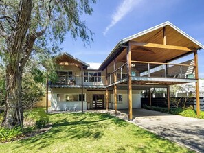 A modern two-story house with a covered patio, a large tree, and a well-maintained lawn.
