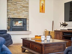 A living room with a stone fireplace, a television mounted on the wall, and a wooden coffee table.