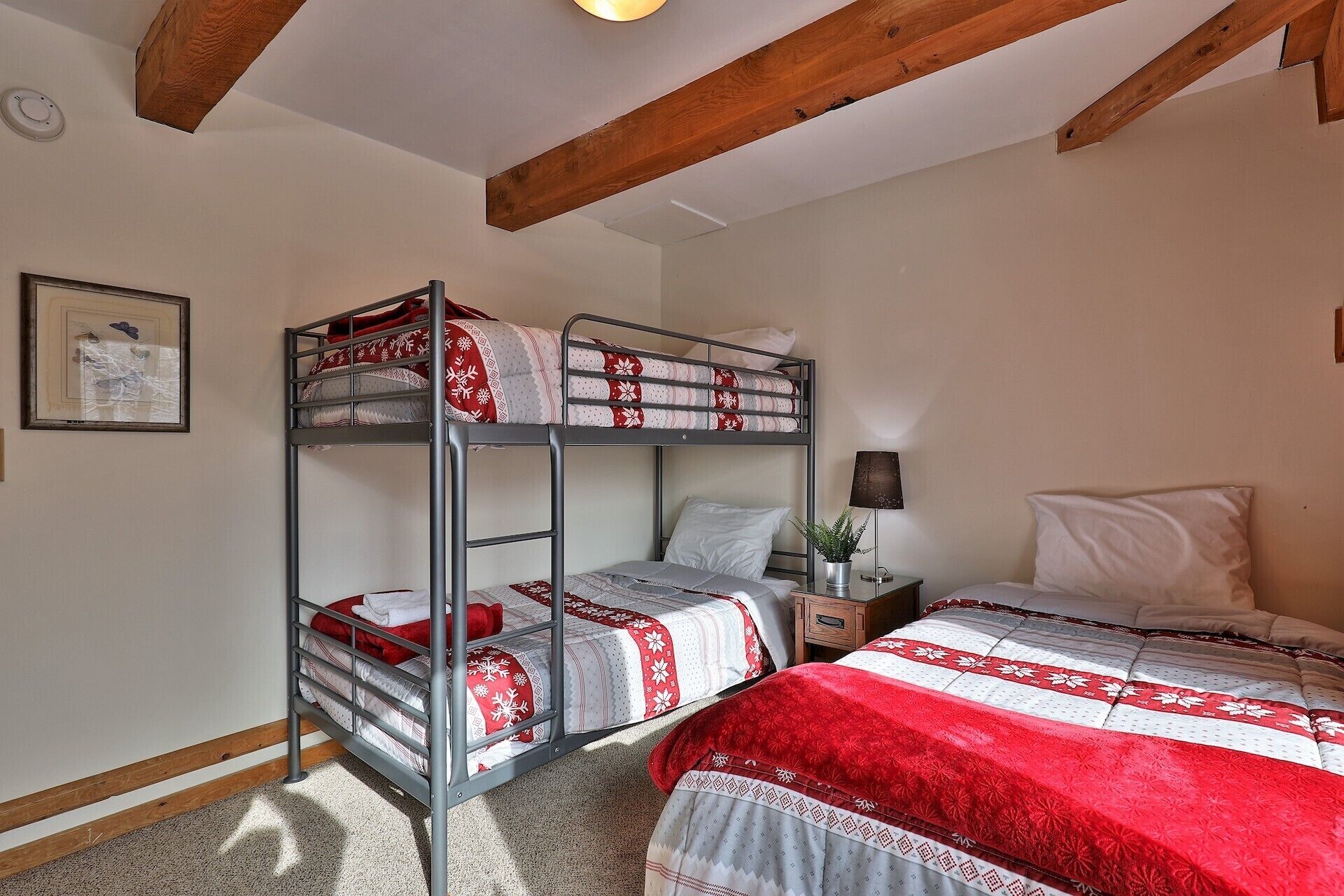 Une chambre avec un lit superposé, un plafond en bois, une table de chevet avec une lampe et un tableau encadré au mur.