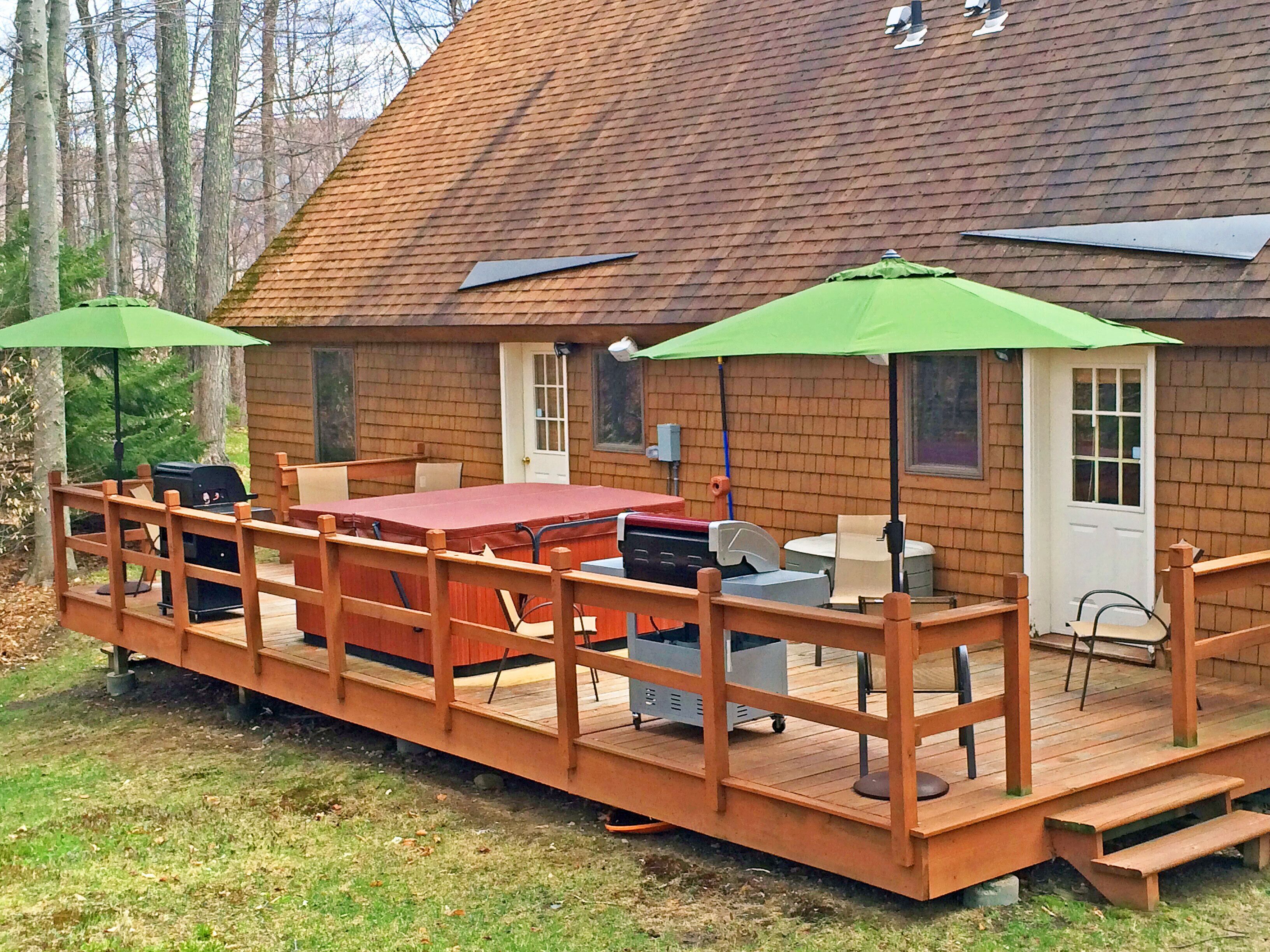 A wooden deck with a table and chairs, a grill, and a covered area with umbrellas.